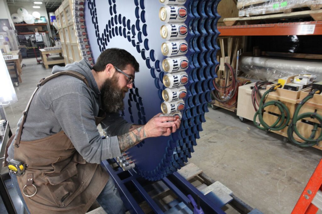 Fabricator building a Miller Lite can wall