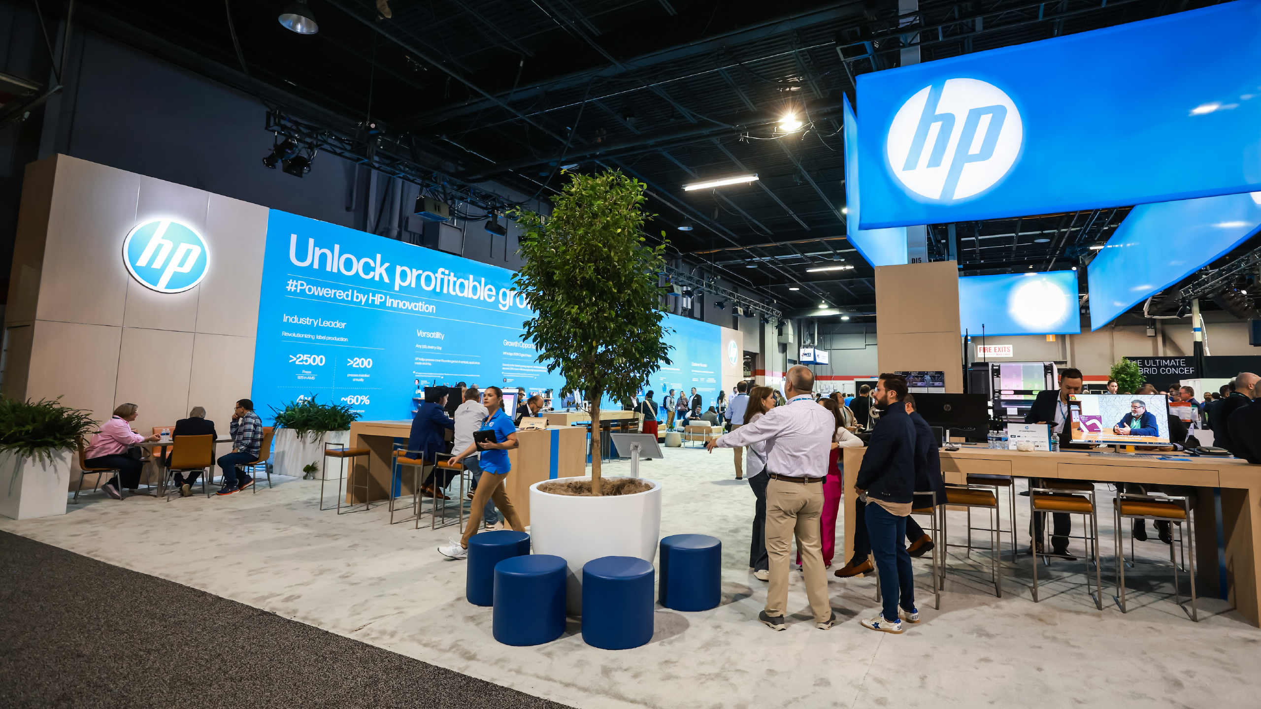 HP booth at Labelexpo Americas with live trees, meeting tables and overhead HP sign, built by Cadence