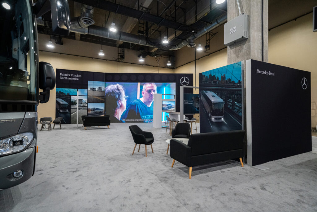 Mercedes-Benz coach exhibit with a motorcoach, lounge seating, and LED wall at a motorcoach industry show